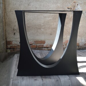 May include: Two black metal table legs with a curved design. The legs are made of steel and have a matte black finish.