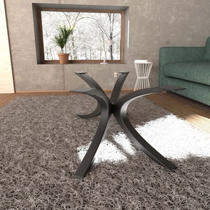 Puede incluir: Una mesa de centro de metal negro con una base curva en forma de X. La mesa est&aacute; sobre una alfombra de pelo gris en un sal&oacute;n.