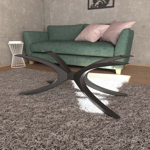Puede incluir: Una mesa de centro de metal negro con una base &uacute;nica en forma de X curvada. La mesa est&aacute; sobre una alfombra de pelo gris en un sal&oacute;n.