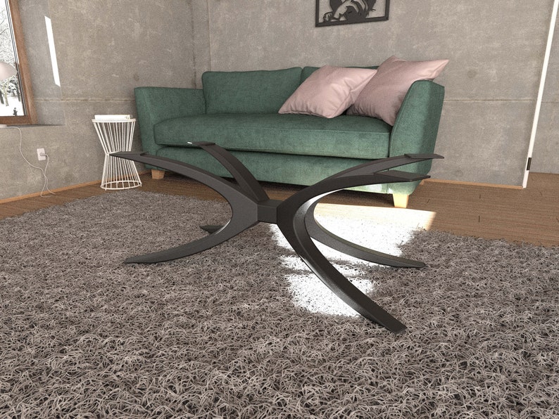 Puede incluir: Una mesa de centro de metal negro con una base &uacute;nica en forma de X curvada. La mesa est&aacute; sobre una alfombra de pelo gris en un sal&oacute;n.
