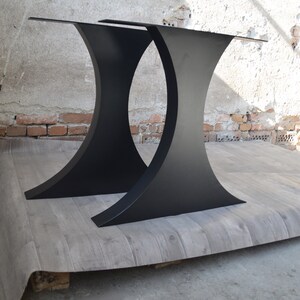 May include: Two black metal table legs with a curved design. The legs are made of thick metal and have a matte black finish.