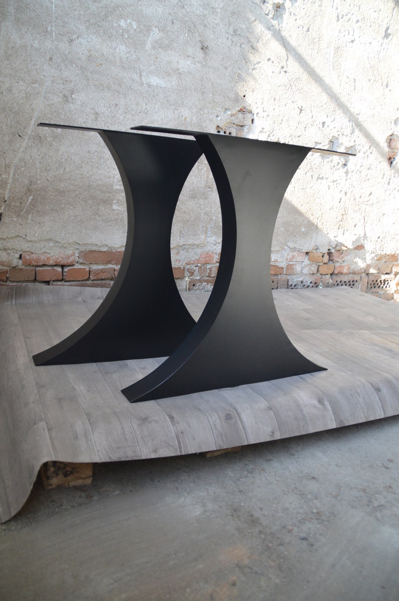 May include: Two black metal table legs with a curved design. The legs are made of thick metal and have a matte black finish.