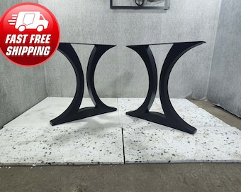 May include: Two black metal table legs with a curved design. The legs are set on a white tiled floor.