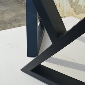May include: Close-up of a black metal table base with a geometric design. The base is made of thick, sturdy metal and has a matte finish.