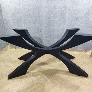 May include: A black, modern table base with a unique, geometric design. The base features six curved legs that intersect in the center, creating a starburst pattern. The legs are made of a solid material and have a matte finish.
