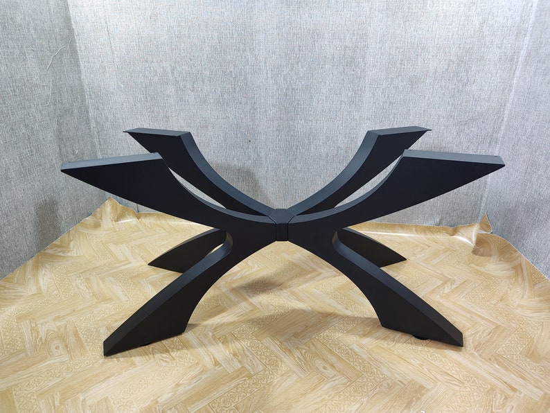 May include: A black, modern table base with a unique, geometric design. The base features six curved legs that intersect in the center, creating a starburst pattern. The legs are made of a solid material and have a matte finish.
