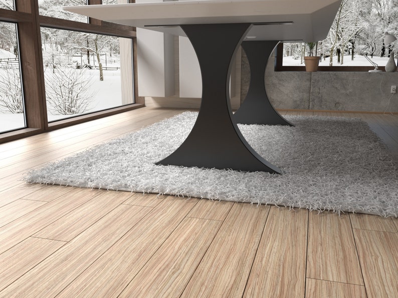 May include: A white table with a black, modern, hourglass-shaped base sits on a white fluffy rug. The table is in a room with a large window overlooking a snowy forest.