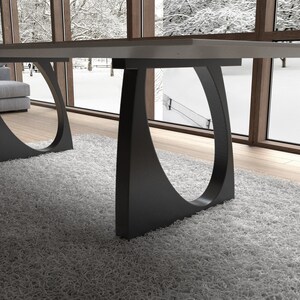May include: A modern dining table with a gray tabletop and black metal legs. The legs have a unique curved design with a circular cutout.