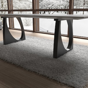 May include: A modern dining table with a white top and black, curved legs. The table is set on a gray rug in front of a window.
