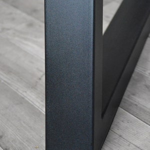 May include: Close-up of a black metal table leg with a textured finish. The leg is square in shape and has a slightly angled design.