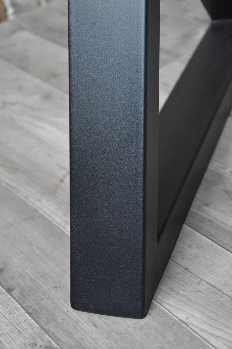 May include: Close-up of a black metal table leg with a textured finish. The leg is square in shape and has a slightly angled design.