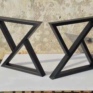 May include: Two black metal table legs with a triangular design. The legs are made of thick metal and have a matte black finish.