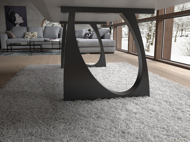 May include: Close-up of a modern table base with a unique curved design. The base is made of black metal and has a sleek, minimalist look. The table base is sitting on a white shag rug.