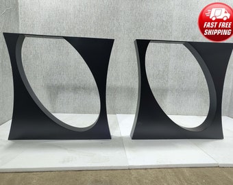 May include: Two black metal table legs with a curved, oval-shaped cutout in the center. The legs are standing on a white surface.