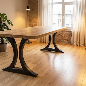 May include: A rectangular dining table featuring a thick, natural light brown wooden top with a smooth grain finish. The table is supported by two distinct, curved black metal legs that flare outward at the base, providing a stable foundation.