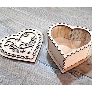 May include: A wooden heart-shaped box with a decorative cutout design. The box is open and the inside is visible. The box is made of light brown wood.