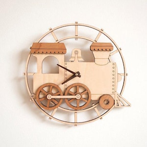 Puede incluir: Reloj de pared de madera con forma de tren. El reloj tiene un acabado en madera clara y presenta un diseño de locomotora con dos ruedas, una chimenea y un marco circular decorativo. Las manecillas del reloj son de color marrón oscuro.