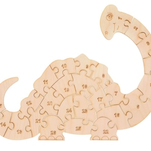 Puede incluir: Un rompecabezas de dinosaurio de madera con 25 piezas. Cada pieza está numerada. El dinosaurio es de color marrón claro y tiene una cara amigable.
