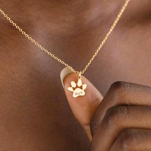 Può includere: Una collana d'oro con un ciondolo a forma di impronta di zampa. L'impronta di zampa ha la parola "Mark" incisa al suo interno.