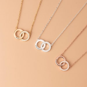 Op de afbeelding: Drie kettingen met in elkaar grijpende cirkels, elk met een andere afwerking: goud, zilver en roségoud. De cirkels zijn versierd met kleine, sprankelende stenen. Elke ketting heeft een delicate ketting.