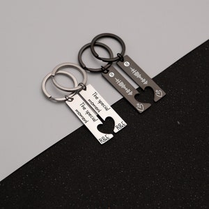 May include: Two silver keychains with matching heart-shaped charms. One keychain has the text "The special moment" engraved on it, while the other has a Spotify code. Both keychains have the letters "R&E" engraved on them.