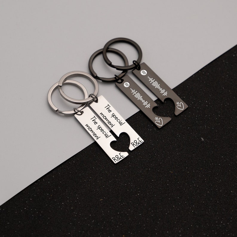 May include: Two silver keychains with matching heart-shaped charms. One keychain has the text "The special moment" engraved on it, while the other has a Spotify code. Both keychains have the letters "R&E" engraved on them.
