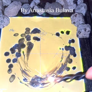 Pode incluir: Obra de arte abstrata sobre um fundo amarelo com tinta cinza escuro formando um desenho circular. O texto "By Anastasia Bulava" está no topo. A obra é cercada por pedras cinzentas.