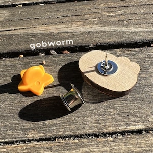 Op de afbeelding: Een houten hartvormige pin met een gouden ster en een zilveren pin achterkant. De pin ligt op een houten oppervlak.