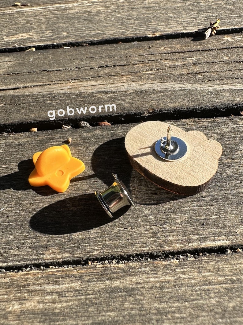 Op de afbeelding: Een houten hartvormige pin met een gouden ster en een zilveren pin achterkant. De pin ligt op een houten oppervlak.