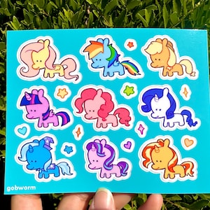 May include: A sheet of colorful pony stickers on a turquoise background. The stickers feature various cartoon ponies with different colored manes and tails, surrounded by stars and hearts. The text "gobworm" is in the bottom left corner.