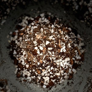 May include: A close-up of a pile of dark brown soil mixed with small white pebbles. The soil is in a container, and the edges of the container are visible.