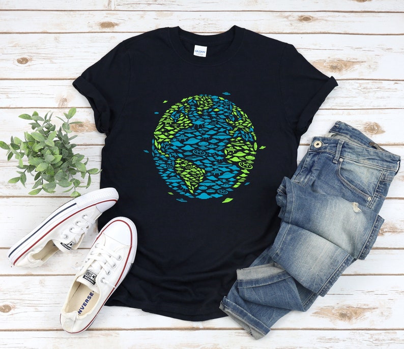 May include: A dark blue t-shirt with a graphic of a green and blue earth made of fish. The shirt is laid out on a white wooden surface with a pair of white sneakers and blue jeans.