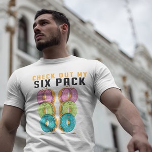 May include: White t-shirt with the text "CHECK OUT MY SIX PACK" in yellow and black. The text is surrounded by six colourful doughnuts with smiling faces.