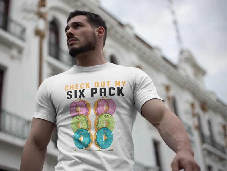May include: White t-shirt with the text "CHECK OUT MY SIX PACK" in yellow and black. The text is surrounded by six colourful doughnuts with smiling faces.