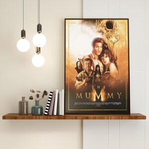 May include: A movie poster for the film "The Mummy" featuring a group of people standing in front of a large, golden statue. The poster has a dark background with a golden border.