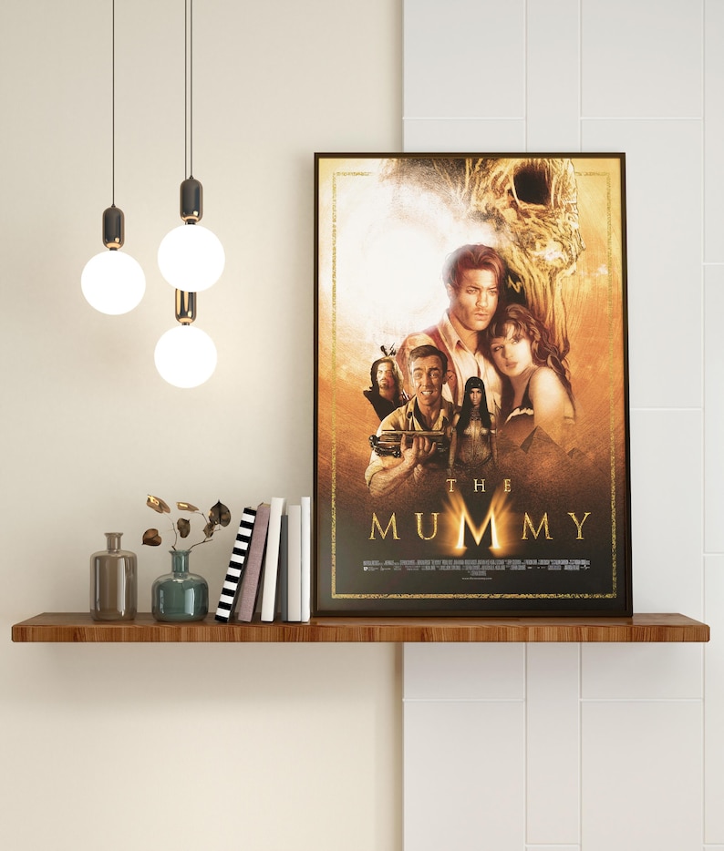 May include: A movie poster for the film "The Mummy" featuring a group of people standing in front of a large, golden statue. The poster has a dark background with a golden border.