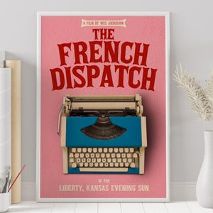 May include: A pink poster with the title "The French Dispatch" in red text. The poster also features a vintage typewriter with a blue body and a cream-colored base. The text "Of the Liberty, Kansas Evening Sun" is at the bottom of the poster.