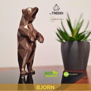 Puede incluir: Una escultura de oso geométrico de color bronce de pie sobre una superficie de madera. La escultura está hecha de muchos triángulos pequeños y tiene un acabado brillante. Las palabras "my TREDDI MADE IN ITALY" son visibles en el fondo.