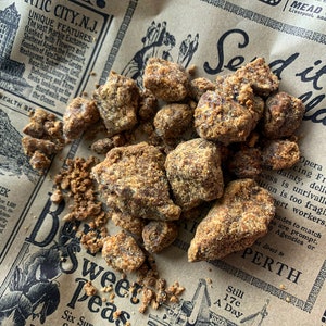 Puede incluir: Un montón de piezas texturizadas de color marrón claro, posiblemente alimentos, se encuentran sobre un fondo de periódico vintage. El periódico tiene texto e ilustraciones descoloridas.