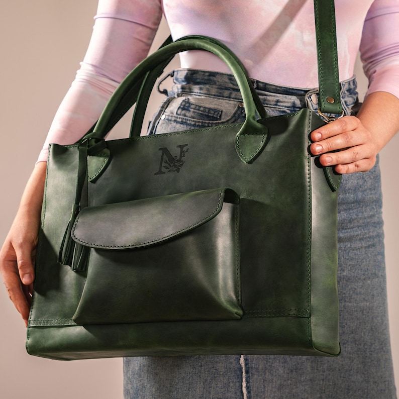 Op de afbeelding: Een donkergroene leren tote bag met een bijpassende schouderriem en handvatten. De tas heeft een voorvak met een flap en een kwastje. De tas heeft een logo op de voorkant. Een stijlvol accessoire.