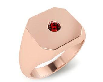 May include: A rose gold signet ring with a red gemstone set in the centre.