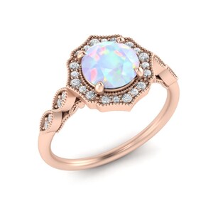 May include: A rose gold ring with a large opal gemstone surrounded by a halo of smaller diamonds. The ring has a delicate, vintage-inspired design.