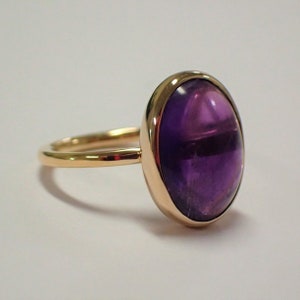Puede incluir: Un anillo de oro con una gran amatista ovalada. El anillo está engastado en una banda sencilla.