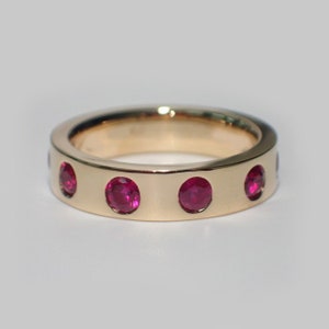 May include: A gold band ring with five red ruby gemstones set into the band.