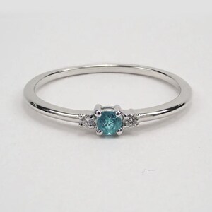 May include: A delicate silver ring with a small, round, teal-colored gemstone surrounded by three smaller, round, white gemstones.