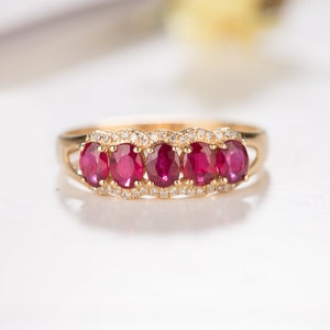 May include: A gold ring with five red oval gemstones and a row of smaller white gemstones around the band.