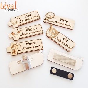 Peut inclure: Plusieurs badges nominatifs en bois avec des symboles de pharmacie gravés et des noms tels que "Léa Préparatrice", "Nicolas Élève préparateur", et "Pierre Pharmacien". Certains badges ont une attache épingle ou magnétique.