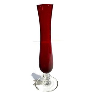 May include: A tall, slender vase with a deep red glass body and a clear glass base. The vase has a flared opening and a rounded bottom.