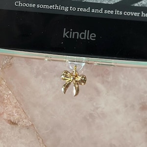 May include: A clear Kindle case with a gold bow charm. The Kindle screen displays the word "kindle" and the text "Choose something to read and see its cover here."