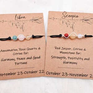 May include: Two handmade Libra and Scorpio zodiac bracelets. The Libra bracelet features aquamarine, rose quartz, and citrine beads. The Scorpio bracelet features red jasper, citrine, and moonstone beads. Each bracelet is on a black cord.